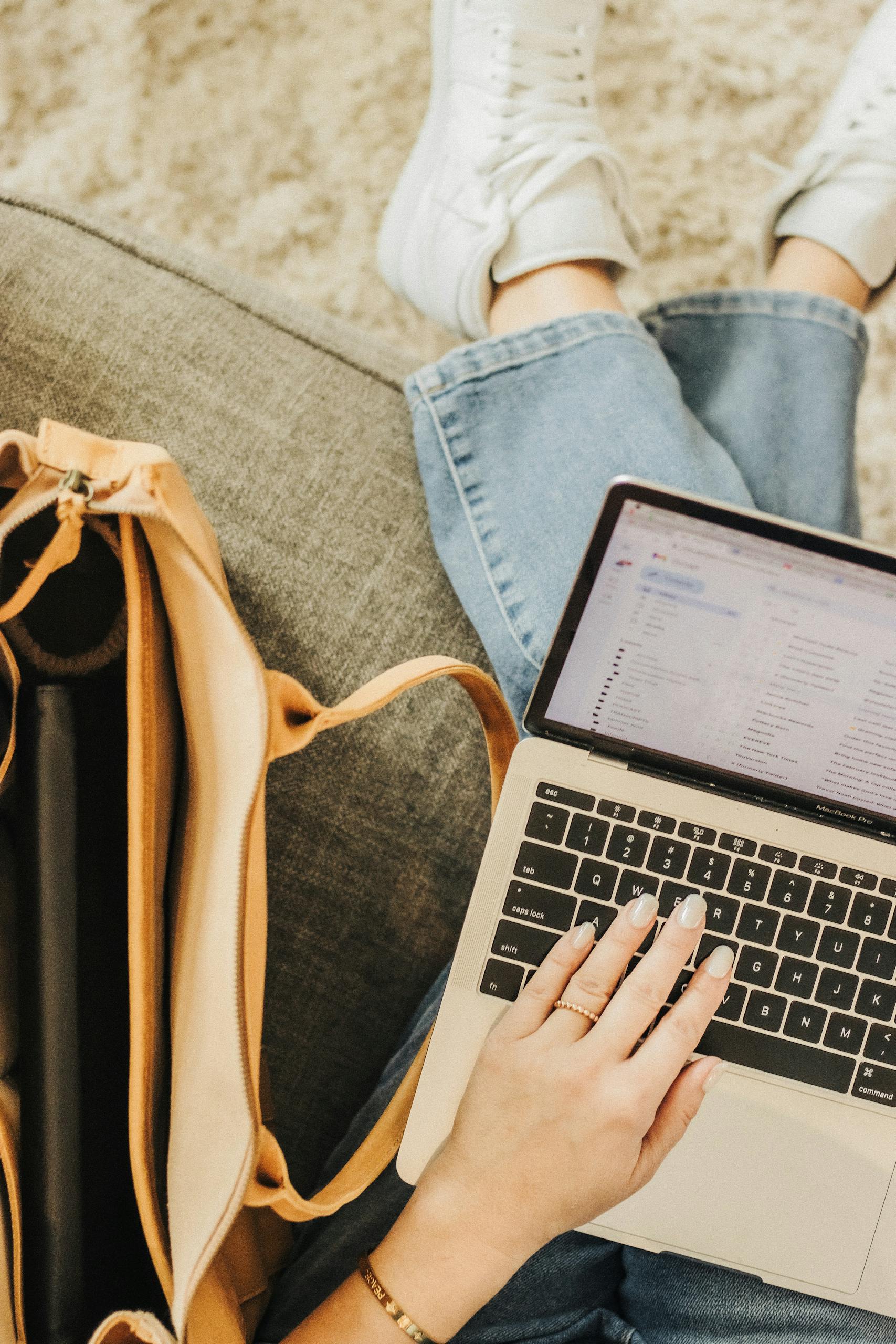 A person using a laptop with an elegant tote bag nearby in a casual setting.