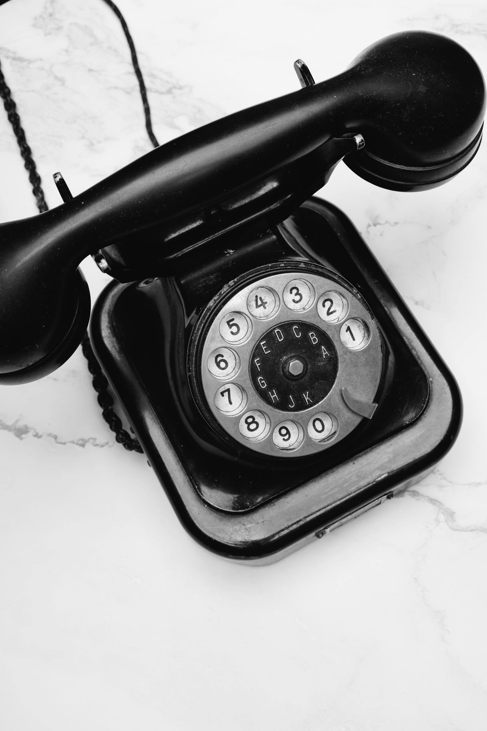 Classic black rotary phone displayed on a marble surface, evoking nostalgia and vintage charm.